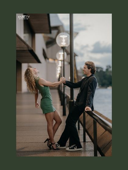 A playful and candid moment from the Sydney shoot. The couple's laughter and dynamic pose capture their fun-loving chemistry against the backdrop of the city lights and water.