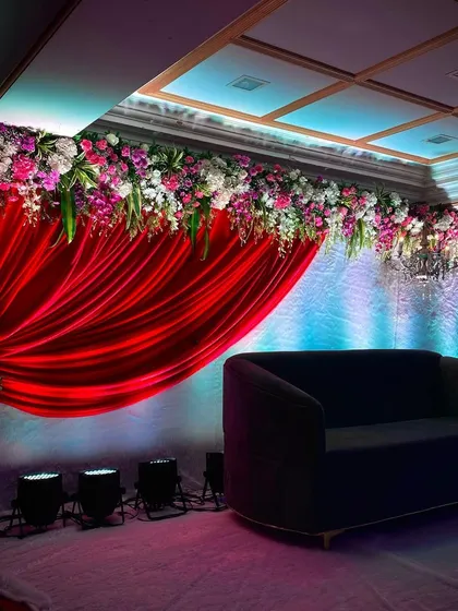 Another angle of the red draped stage, showing how the lighting highlights the floral arrangement and the seating area. This is a popular choice for evening events.