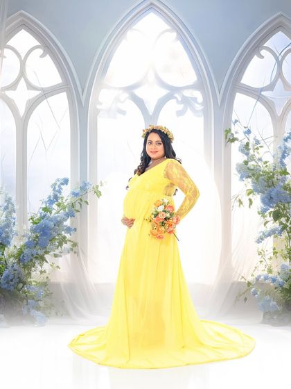 A serene solo portrait of the mother-to-be in a bright yellow gown. The backdrop features ethereal white window arches and blue flowers, creating a heavenly, dream-like atmosphere.