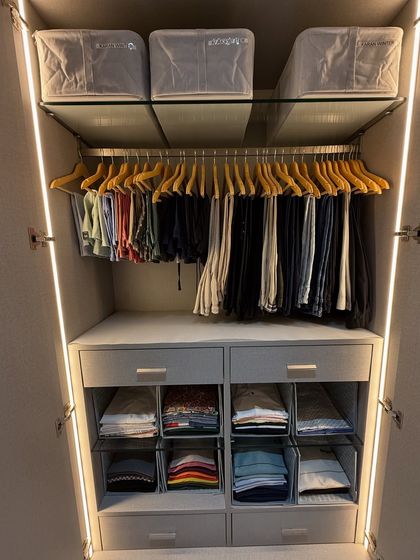 A beautifully organized closet featuring wooden hangers for trousers and clear dividers for folded clothes. Using consistent hangers and storage solutions creates a clean, streamlined look that is simple to maintain.