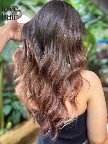 The stylist's hand showcases the soft texture and beautiful color melt of this unique rose gold balayage.
