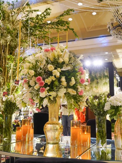 A close-up of a table centerpiece, featuring a beautiful arrangement of white and pink flowers in a golden vase, surrounded by warm candlelight.