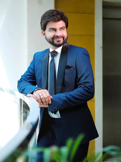 A relaxed and smiling portrait of the groom. The natural, soft lighting from the window creates a pleasant and inviting look.