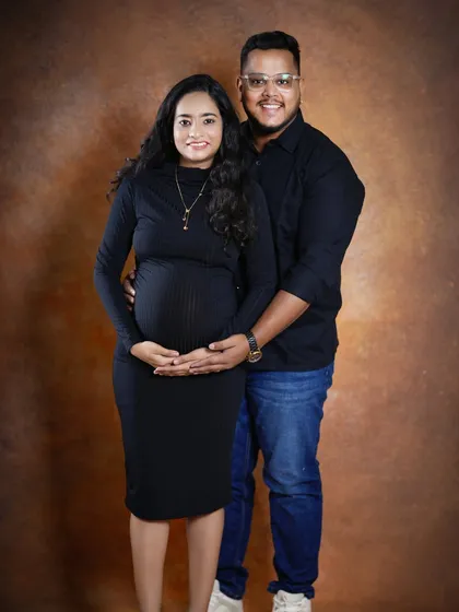 A warm and classic studio portrait of the couple. They stand together, both looking at the camera, creating a beautiful formal memory of their pregnancy.