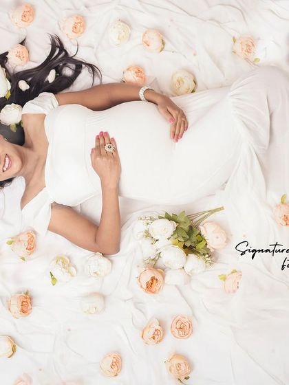 A dreamy overhead shot of the mother-to-be in a white gown, surrounded by a bed of roses.