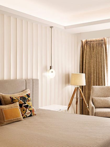 The master bedroom in our "In the Heart of Mumbai" project features a neutral color palette of white and beige, with subtle fluted paneling behind the bed for a touch of texture.