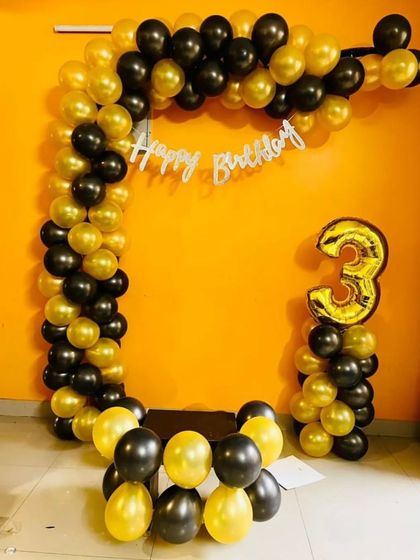A 3rd birthday decoration with a black and gold semi-arch and a number '3' balloon pillar.