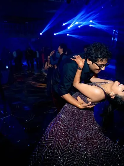 The couple shares a romantic dip on the dance floor during their sangeet, surrounded by dramatic blue lighting.