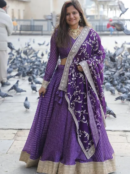 A full-length shot of the purple bandhani-style lehenga. The embroidered dupatta adds a layer of richness to the traditional printed skirt.