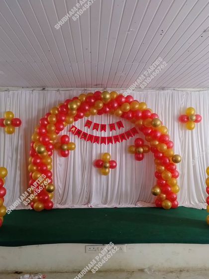 A simple stage setup with a red and gold balloon arch against a white curtain.
