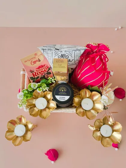 A top-down view of the macrame tray hamper. This one includes golden flower T-light holders, snacks, and a bright pink potli.