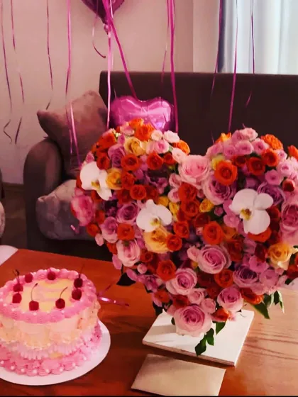 Perfect for anniversaries or a grand romantic gesture, this heart-shaped arrangement is overflowing with a mix of colorful roses and orchids. It’s designed to be a stunning centerpiece, shown here next to a birthday cake to complete the celebration.