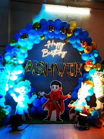 A royal first birthday for a little prince. The decoration features a castle-themed backdrop, a blue and gold balloon arch, and a light-up marquee number '1'.