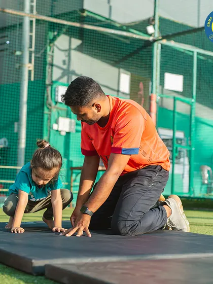 A coach guides a very young gymnast through the beginning stages of a forward roll, emphasizing safety and proper form from day one.