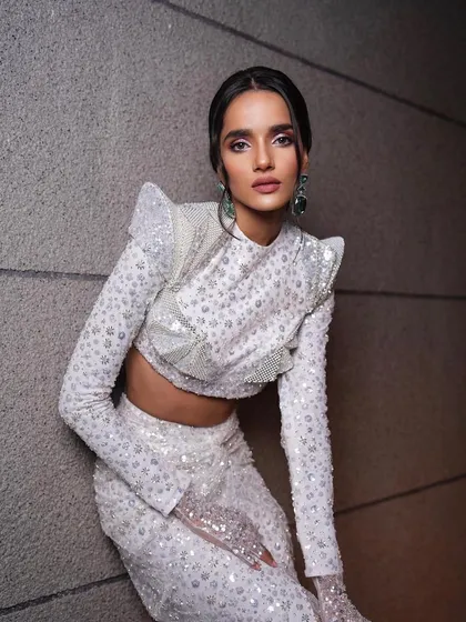 A modern and futuristic look. The makeup is clean and graphic, with a focus on a flawless base, complementing the unique, structured white outfit.