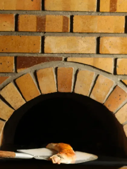 A pizza being carefully removed from our brick wood-fired oven. This traditional cooking method is key to achieving the perfect crispy crust and smoky flavour.