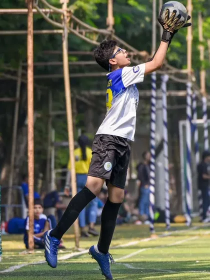A young goalkeeper leaps high to confidently claim the ball during a match. This dynamic shot is a tribute to the crucial role our goalkeepers play in the team's success.