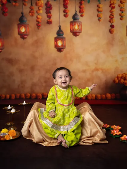 This baby's joyful expression is infectious in this Diwali themed sitter session. The vibrant green outfit contrasts beautifully with the warm, festive background.