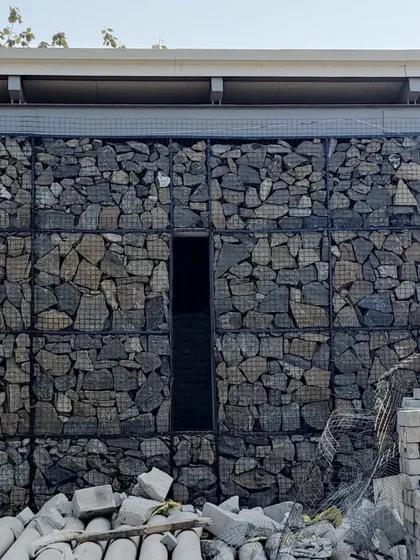 A narrow, monolithic doorway is carved into a massive gabion wall at our Alibaug project. This creates a sense of mystery and passage, contrasting the solid, heavy wall with the dark, inviting void.