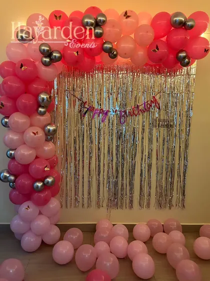 A simple L-shaped balloon garland in pink and silver against a fringe backdrop. This is a great way to decorate a small wall space at home.
