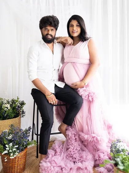 A stylish portrait of an expecting couple. The mom-to-be glows in her pink gown while her partner sits casually beside her.
