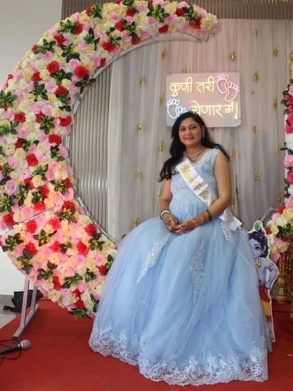 A princess moment at her baby shower. This mom-to-be is all smiles, seated on a floral moon decoration in a lovely blue ball gown.