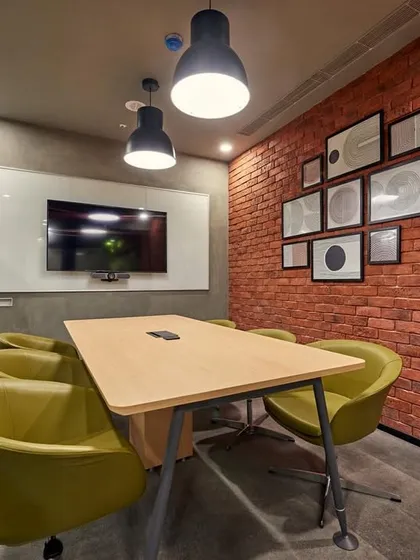 An intimate meeting room with an exposed brick wall and comfortable green armchairs. The space feels more like a cozy study than a corporate meeting room.