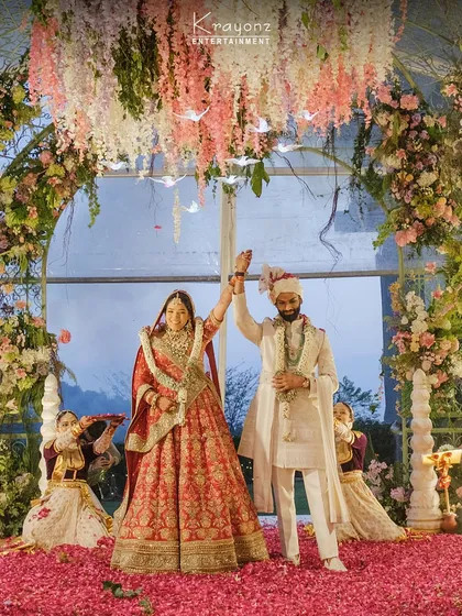 A beautiful moment of celebration as the couple stands together under a floral arch. The ground covered in pink petals adds to the romance of this perfect wedding day scene.