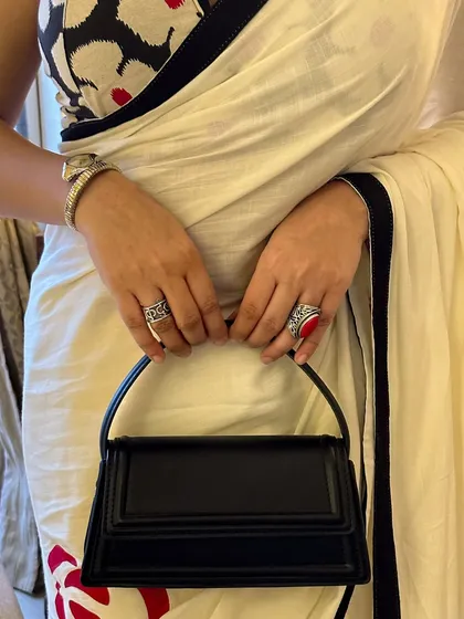 A close-up on the accessories. The structured black bag, silver watch, and statement rings add layers of texture and personality to the hand-painted saree look.
