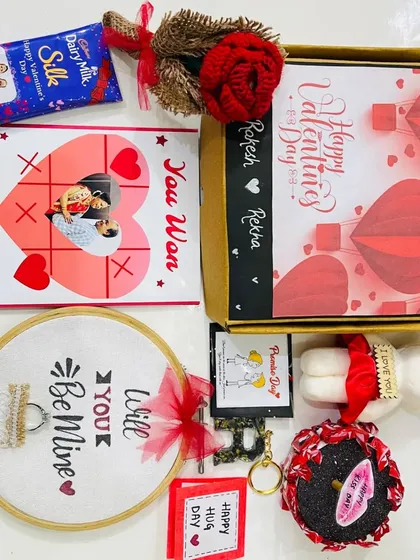 A creative and playful Valentine's hamper. It includes a "You Won My Heart" tic-tac-toe frame, a "Will You Be Mine" embroidery hoop, a teddy bear, and personalized chocolates.