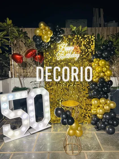 A spectacular 50th birthday party on a terrace, designed for a memorable night-time celebration. This setup features a brilliant gold sequin backdrop, a custom neon sign, large light-up '50' marquee numbers, and a dramatic black and gold balloon arrangement.