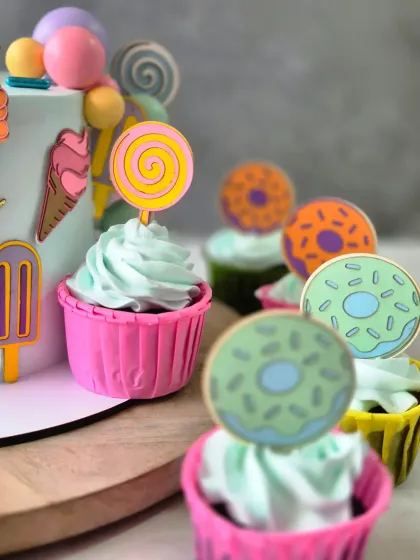 A closer look at the matching cupcakes for the Candy Land theme. Each one is topped with light whipped cream frosting and a cute, edible topper like a lollipop or donut.