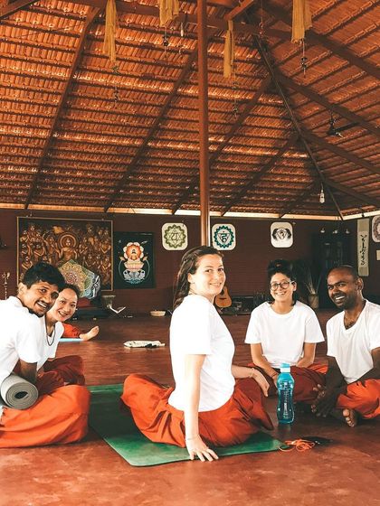 Students relax together in the shala, tired but happy after a practice session. The yoga hall becomes a second home, a space of comfort, challenge, and shared experience.