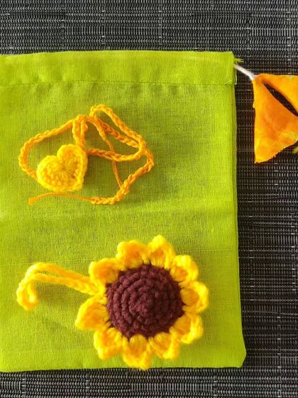 A simple and sweet Rakhi gift set, featuring a sunflower rakhi and a heart-shaped tie, presented in a lovely green pouch.