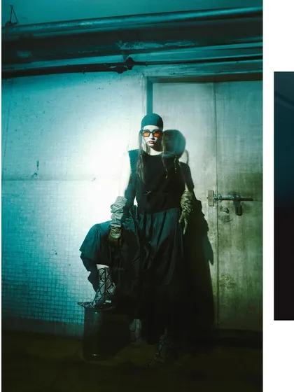 This image is bathed in a cool, teal-colored light, giving the scene a futuristic or dystopian feel. The model stands on a metal bin, adding to the industrial aesthetic.