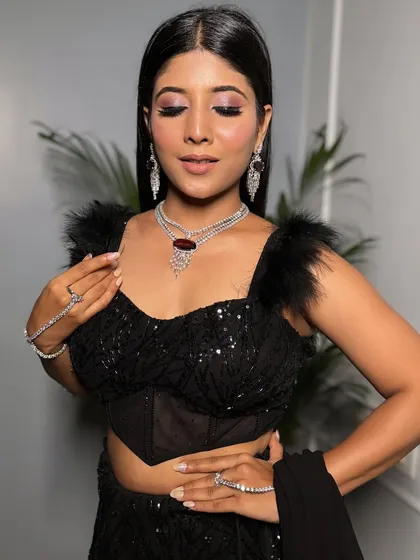 A full view of the dramatic black sequin and feather outfit. The look is completed with a sparkling zircon and ruby necklace and matching hath phool, perfect for a high-glamour event.