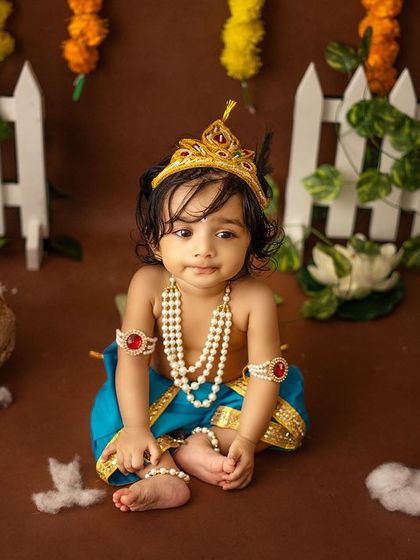 A curious baby Krishna looks at the camera, surrounded by all the elements of a traditional Janmashtami celebration.