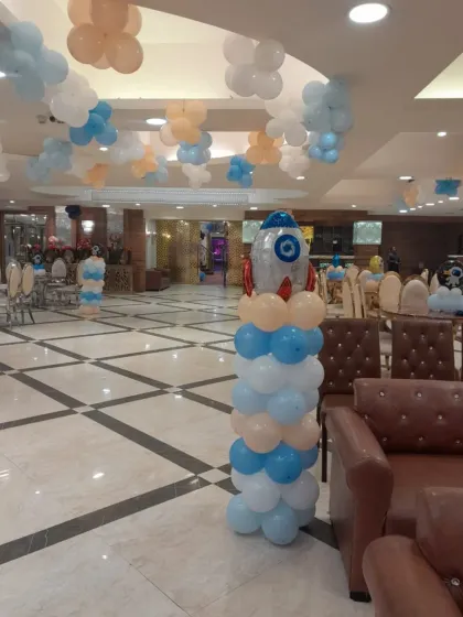 A rocket ship balloon pillar and cloud-like balloon bunches on the ceiling work together to create an immersive space theme throughout the entire banquet hall.