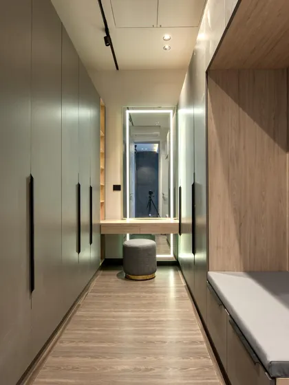 A modern walk-in closet and dressing area with a built-in vanity and mirror. The combination of wood and grey cabinetry creates a warm yet contemporary feel.
