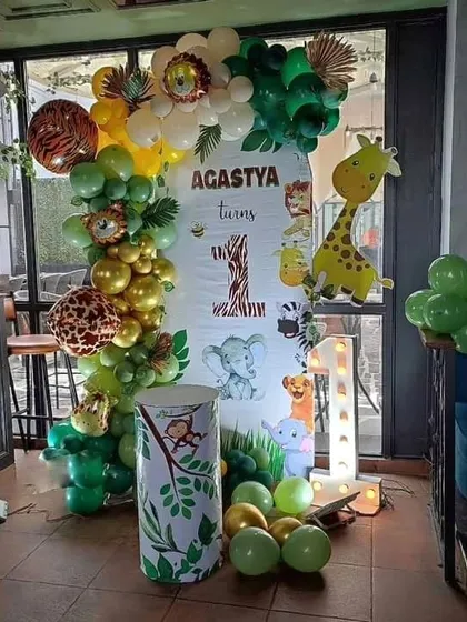 A safari adventure for Agastya's first birthday. This setup features a personalized backdrop with jungle animals, an organic balloon garland with animal-print balloons, and a light-up number '1'.
