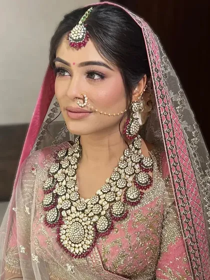 A close-up portrait of a bride with a soft, romantic updo. The hairstyle is designed to look beautiful under a dupatta and with heavy bridal jewellery.