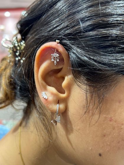 A cute silver styling idea, featuring a delicate hanging in the helix, a wing stud, and a bow-shaped hoop. This shows how to create a themed look with different pieces.