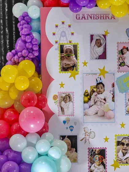 A close-up of a milestone board from a carnival-themed first birthday. The board is decorated with photos from the baby's first year, surrounded by colorful balloon art.