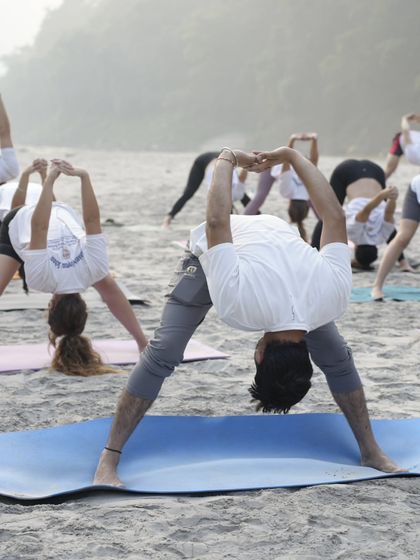 A group session on the beach, where we are all practicing a wide-legged forward bend. Practicing outdoors adds a different dimension to our yoga, helping us feel more grounded and connected to the environment.