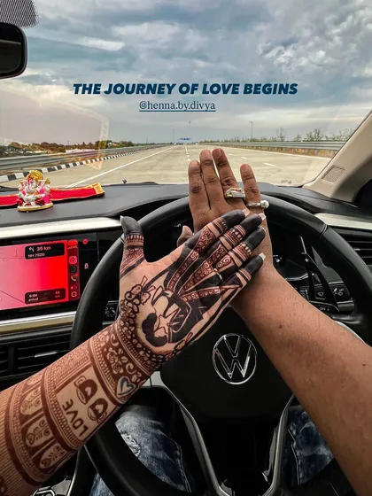 A creative shot showcasing the rich henna stain. The couple's hands are placed on a steering wheel, symbolizing the beginning of their journey of love together.