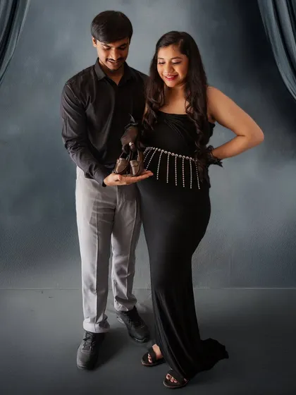 A classic and sweet announcement photo. The couple holds up a pair of tiny baby shoes, a timeless symbol of the new life they are waiting for.