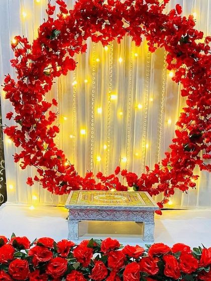 A circular arch of red cherry blossoms against a curtain of fairy lights. The base is lined with red roses, creating a simple yet striking decoration ready for any festival.