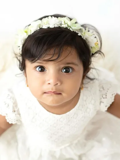 A close-up of a sweet six-month-old girl in a white lace dress. Her direct gaze and innocent expression make for a captivating portrait.