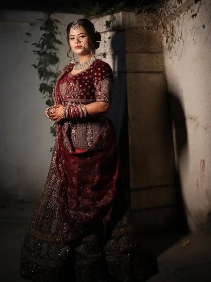 A full-length shot in a moody setting, highlighting the richness of the bride's velvet lehenga and her confident pose.