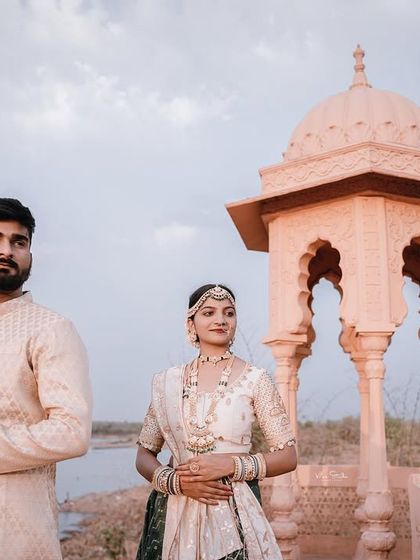 A medium shot of the couple on the balcony, with the water and distant shore in the background. Their traditional attire and the historic setting combine to create a beautiful and timeless portrait.